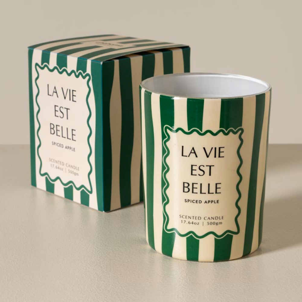 A scented candle in a green and cream striped tin with a matching box, labeled 'LA VIE EST BELLE' and 'SPICED APPLE'.
