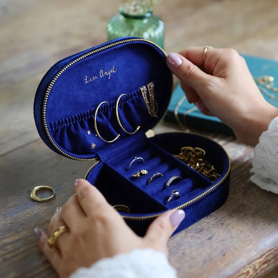 Blue jewelry case with gold jewelry held by a person on a wooden surface