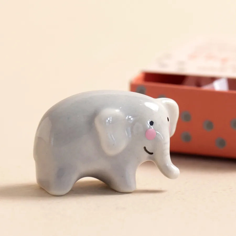 Gray elephant figurine with rosy cheeks on a beige background.