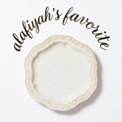 An off-white ceramic shallow dish with a scalloped, fluted rim, shown on a white background with the text 'alafiyah's favorite' written in brown script above it.