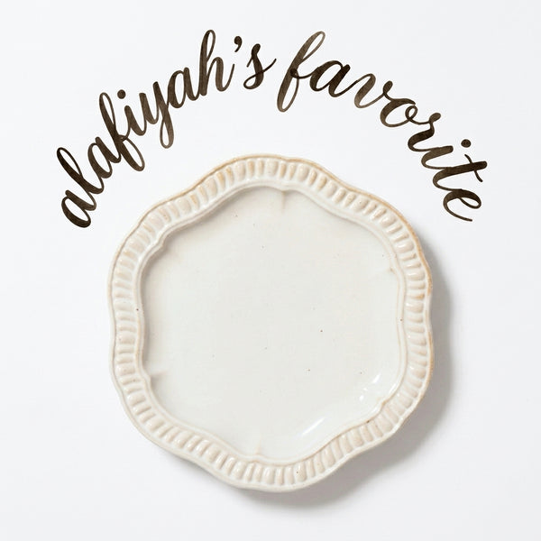 An off-white ceramic shallow dish with a scalloped, fluted rim, shown on a white background with the text 'alafiyah's favorite' written in brown script above it.