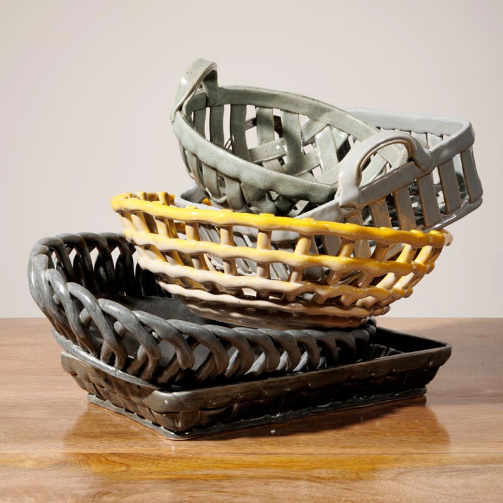 Three nested woven ceramic baskets in gray, tan, and black, stacked on a wooden surface against a plain light background.