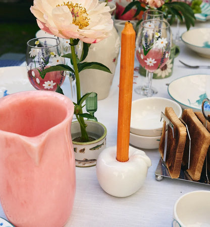 Pink ceramic jug and floral-painted wine glasses on breakfast table with candle holder, toast rack and peony flower.