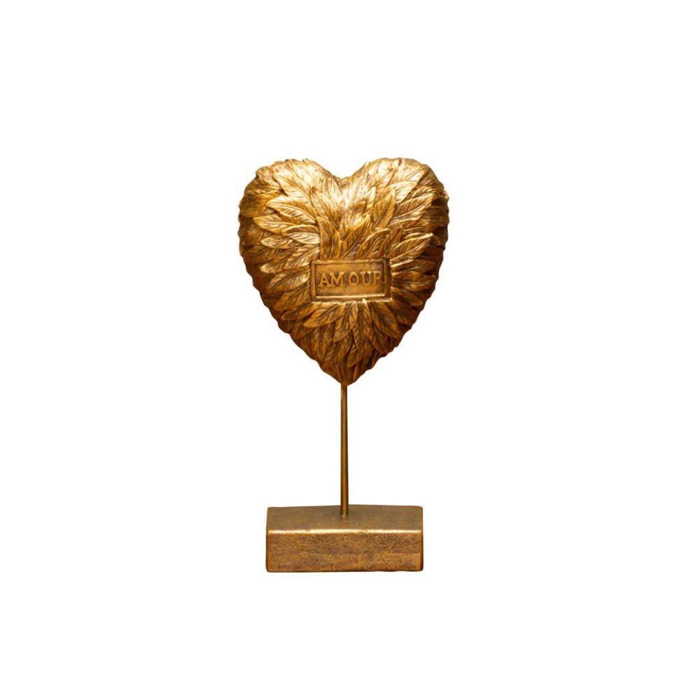 A gold heart-shaped decorative sculpture with a textured, feather-like surface and a small central plaque reading 'AMOUR', mounted on a thin vertical stem over a rectangular base, shown against a plain white background.