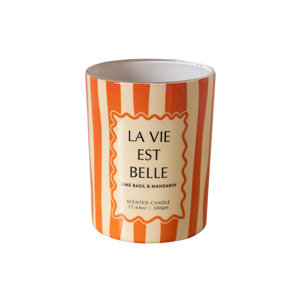 A cylindrical scented candle with a white and orange striped design, featuring a central cream-colored label with the French text 'LA VIE EST BELLE' and smaller scent details 'LIME BASIL & MANDARIN'.