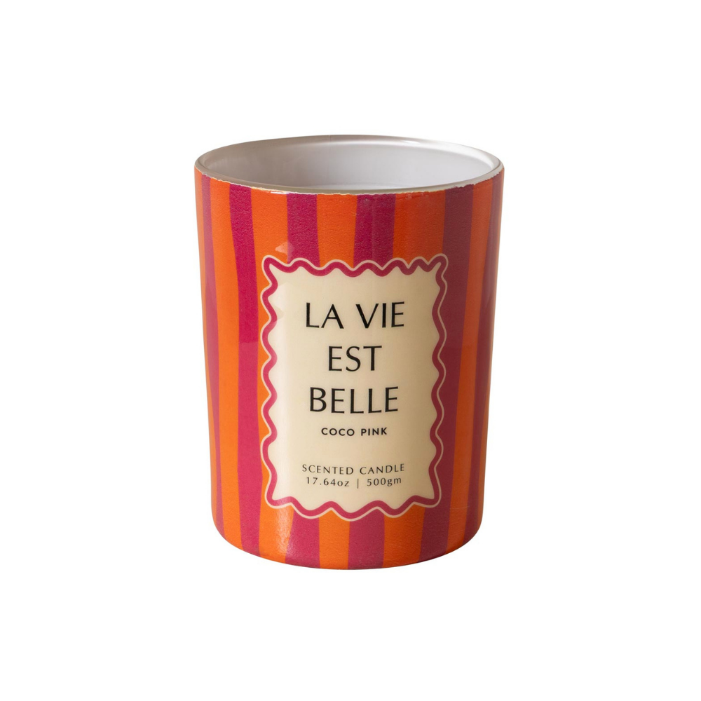 A cylindrical scented candle in a striped container with orange, pink, and red vertical stripes, featuring a cream-colored label with the French text 'LA VIE EST BELLE' and 'COCO PINK'.
