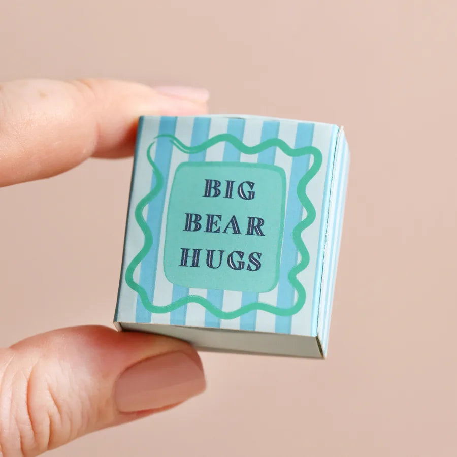 Small box with 'Big Bear Hugs' text held between fingers against a beige background