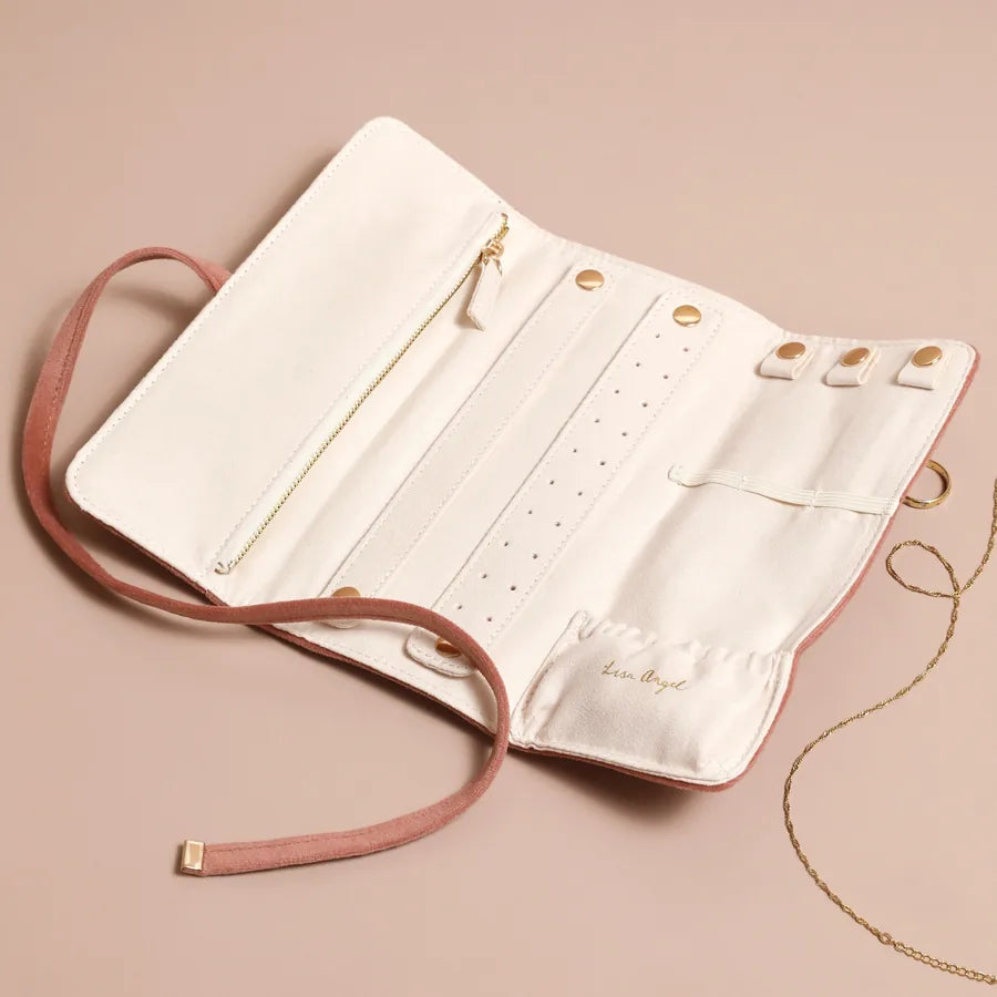 An off-white faux leather jewelry organizer roll with a dusty pink faux suede strap and gold-tone hardware, shown open on a solid beige background with a gold chain draped over it.