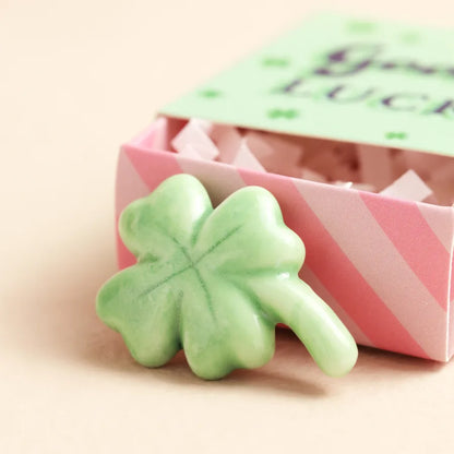 Green four-leaf clover-shaped candy in a pink box with a green bow on a beige background