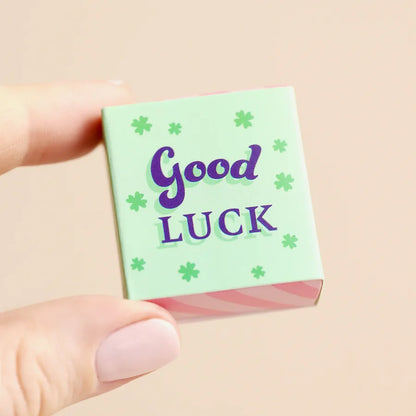 Small green card with 'Good Luck' text held by a hand on a beige background