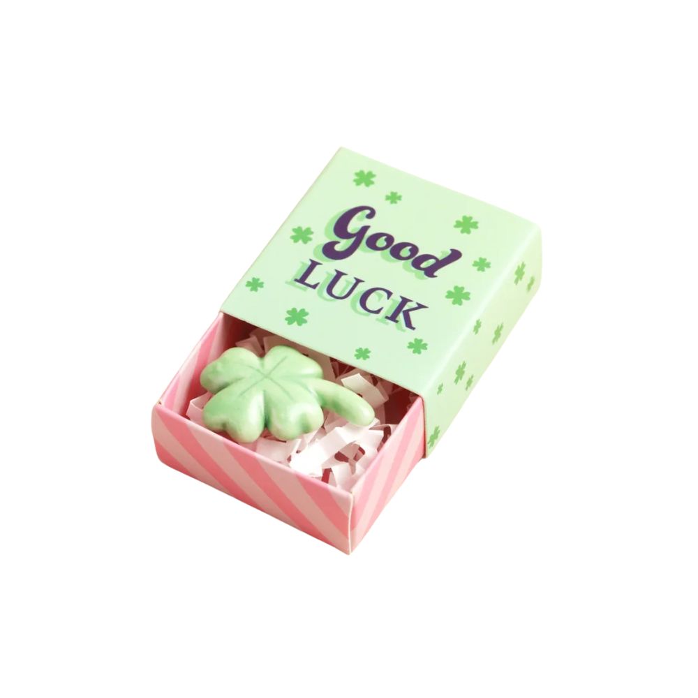 A small St. Patrick's Day themed matchbox gift box with a light green lid that reads 'Good Luck' in purple lettering, decorated with green shamrock motifs.