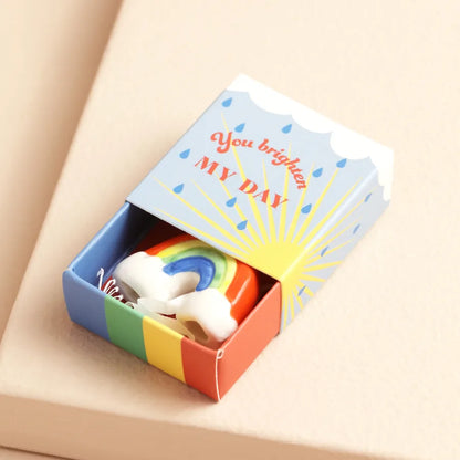 Colorful matchbox with rainbow design and 'You brighten my day' text on a beige background.