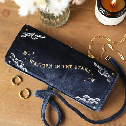 Navy blue pouch with 'WRITTEN IN THE STARS' text on a wooden surface with decorative items.