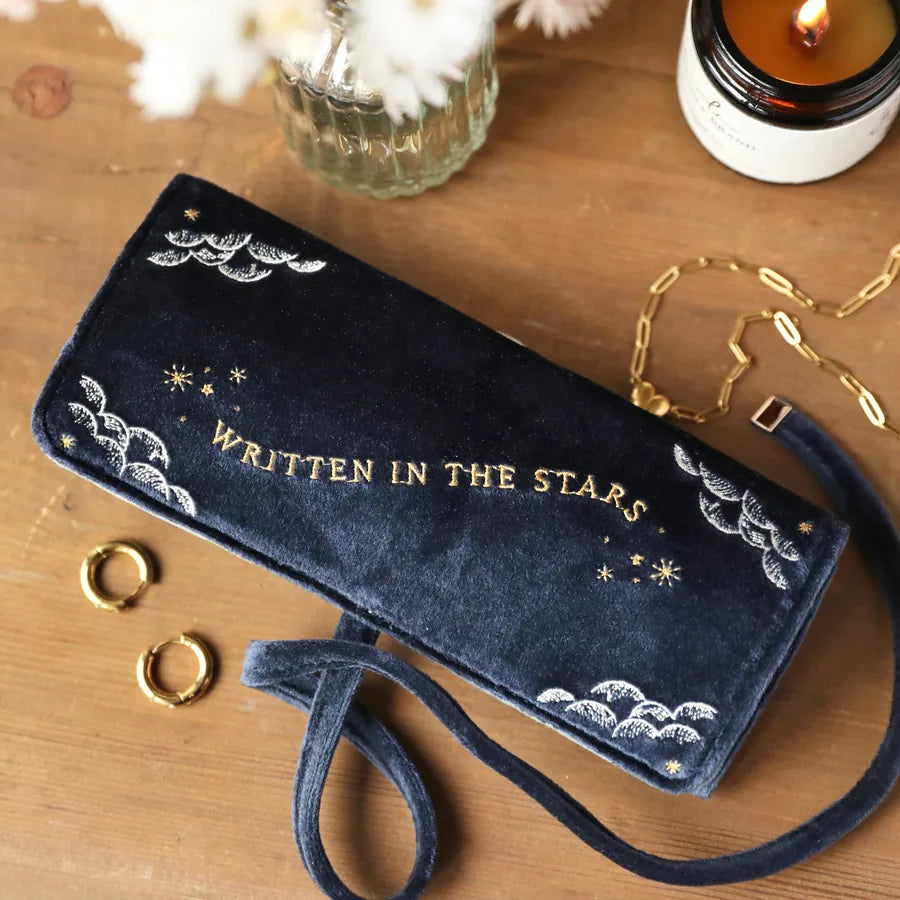 Navy blue pouch with 'WRITTEN IN THE STARS' text on a wooden surface with decorative items.