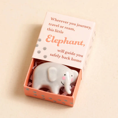 Small elephant figurine in a decorative matchbox with a message on a beige background.
