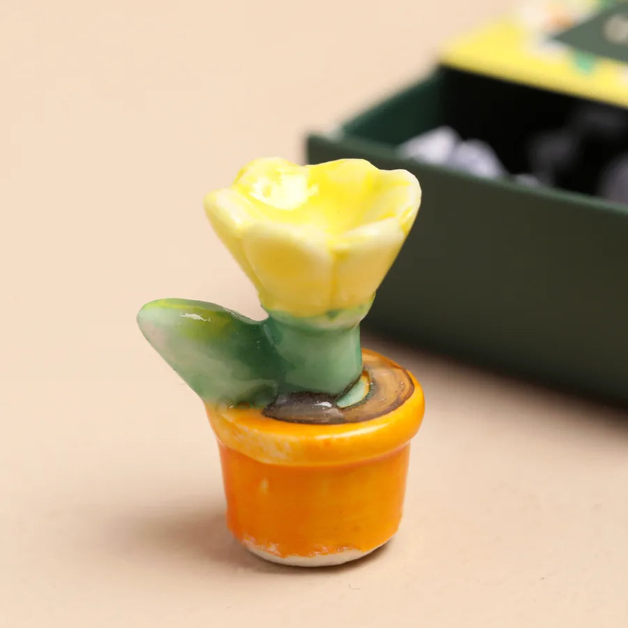 Small ceramic flower pot with a yellow flower on a beige surface.