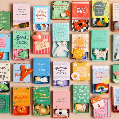 Collection of small decorative matchboxes with various messages and illustrations on a wooden surface.