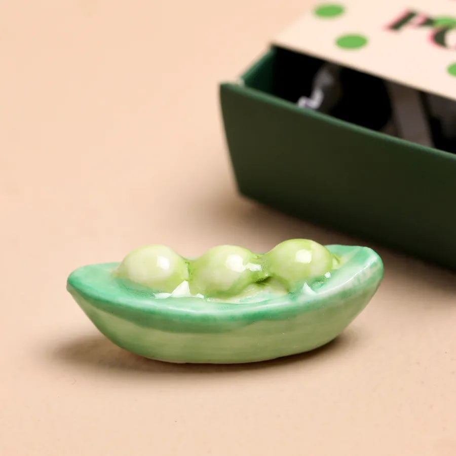 Small decorative ceramic peapod on a beige surface with a blurred background