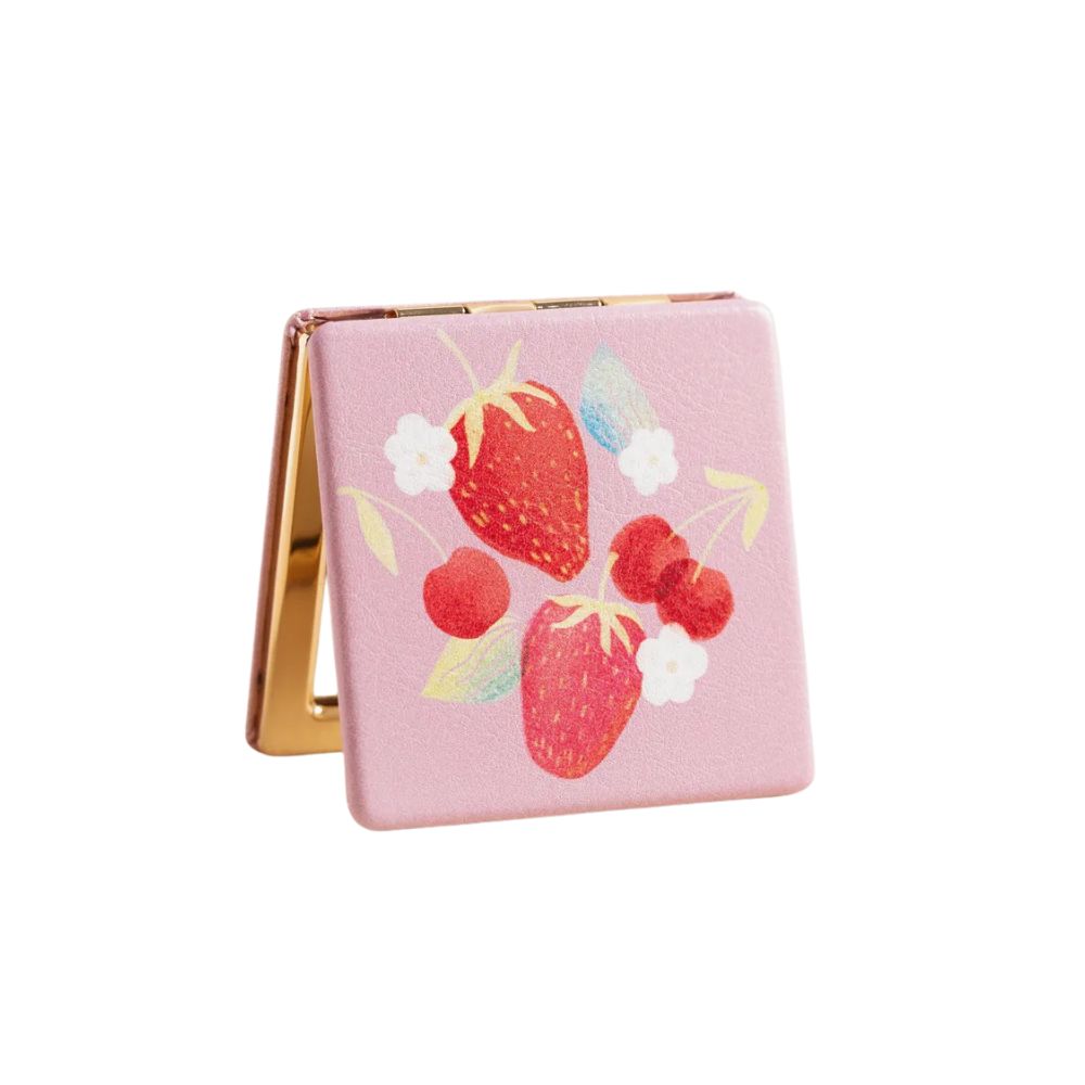 A square pink compact mirror with a gold-tone hinge and a printed design of strawberries, cherries, and small white flowers on the front, shown open against a plain white background.