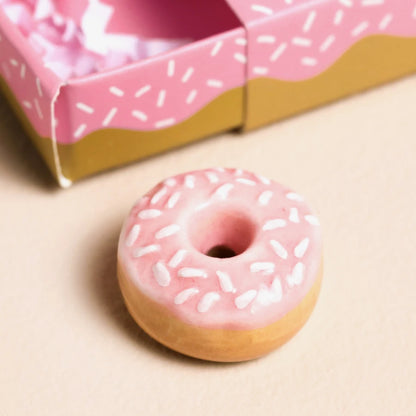 Pink frosted donut with sprinkles on a beige surface