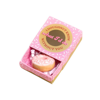 A novelty donut-shaped item displayed inside a pink gift box with a printed lid. The box has a pink sprinkle pattern and a gold circular label reading, 'I DOUGHNOUT KNOW what I'd do WITHOUT YOU.