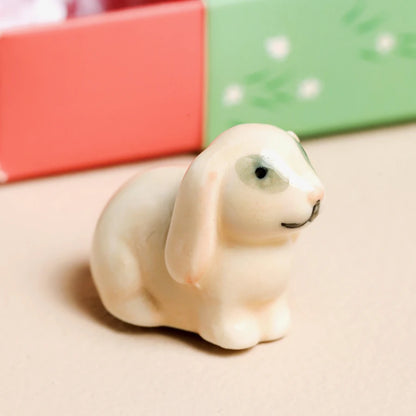 Small white dog figurine on a beige surface with colorful gift boxes in the background