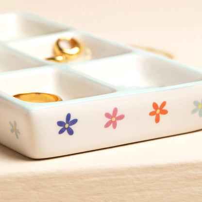White ceramic jewelry organizer with floral designs on a beige surface.