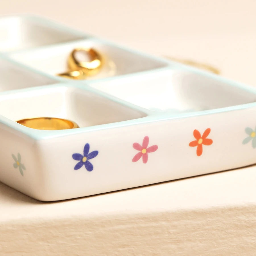 White ceramic jewelry organizer with floral designs on a beige surface.