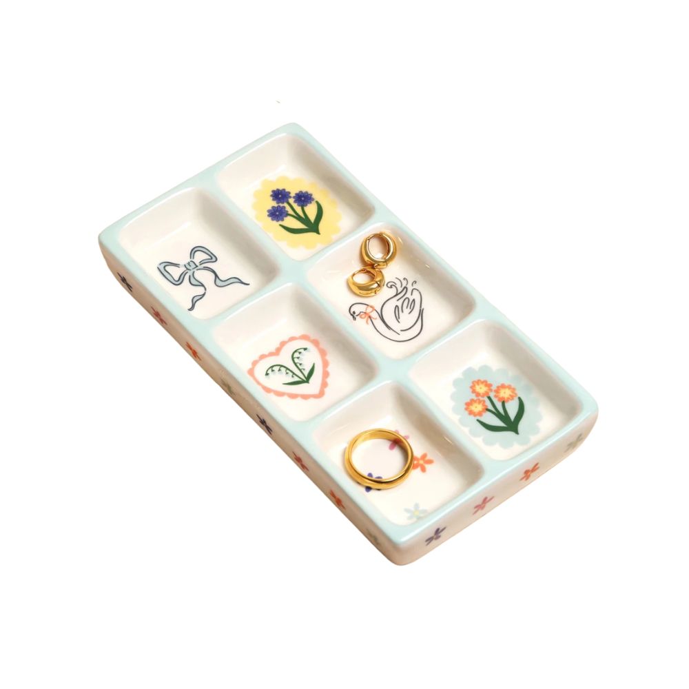 A rectangular ceramic ring tray with six compartments, decorated with pastel floral and bow motifs in a light blue-green and cream color scheme, shown on a plain white background.