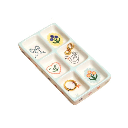 A rectangular ceramic ring tray with six compartments, decorated with pastel floral and bow motifs in a light blue-green and cream color scheme, shown on a plain white background.