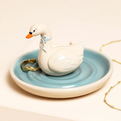White swan-shaped trinket dish with a blue base on a beige background