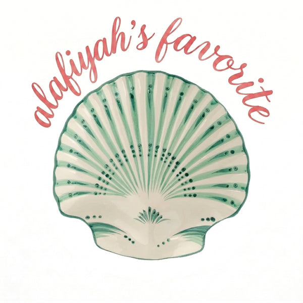 A decorative shell-shaped plate or dish in off-white with green radial patterning, centered on a white background with the phrase 'alafiyah's favorite' written in coral script above it.
