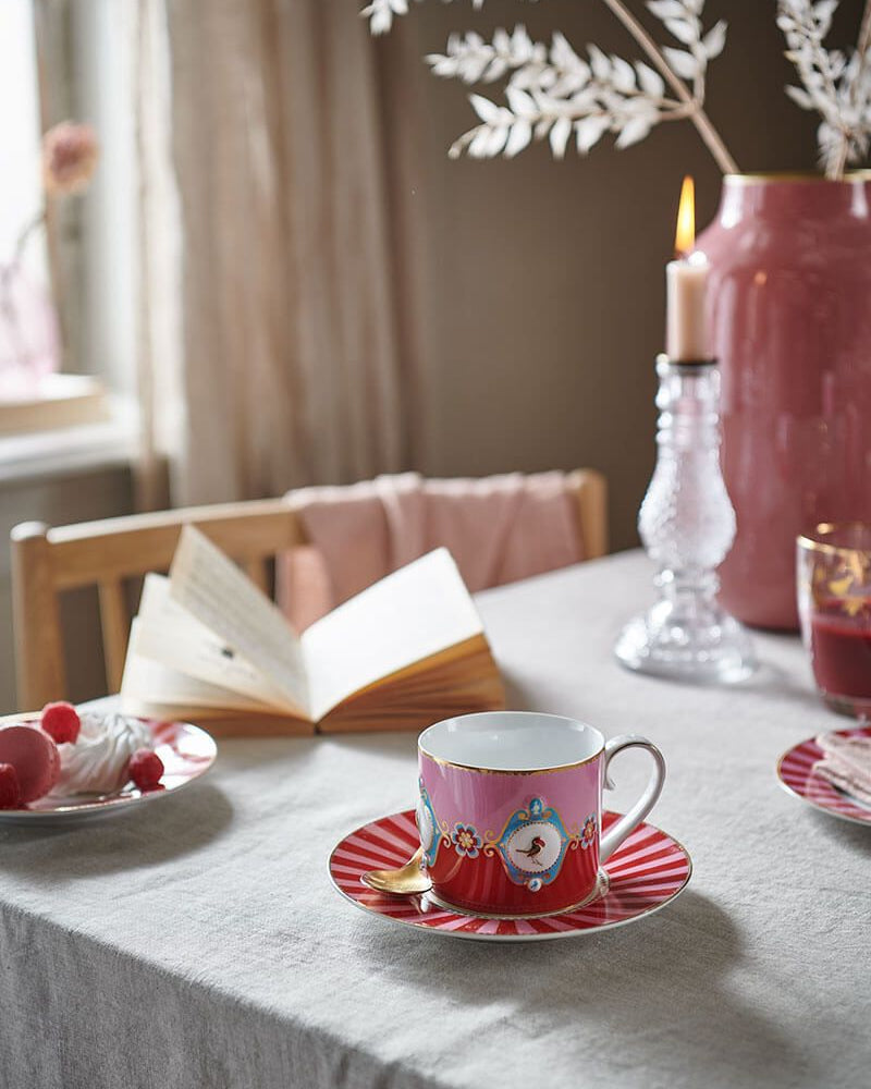Table setting with a pink teacup and saucer, book, and candle in a cozy room.
