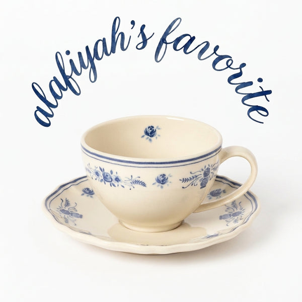 A cream-colored ceramic teacup and saucer with blue floral patterns, set against a white background with the text 'alafiyah's favorite' written in blue script above it.