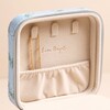 A close-up of a beige fabric organizer pouch with multiple zippered compartments and loops, set against a very light blue background.